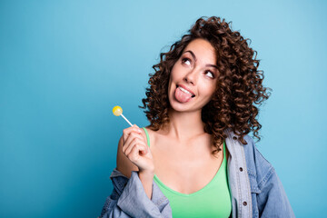 Obraz premium Photo of funny girl youth hold lollipop look copyspace think thoughts imagine tasty yummy dessert show tongue out wear green tank-top isolated over blue color background