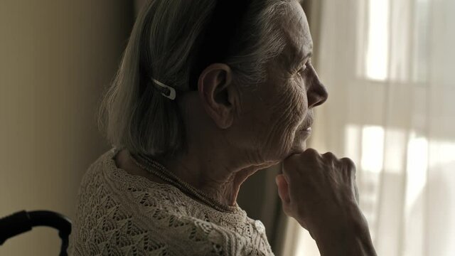 Senior woman sit on wheelchair and looks through the window