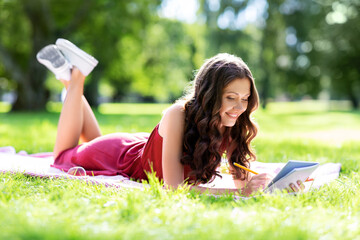 leisure, inspiration and people concept - happy smiling woman writing to diary or notebook lying on...