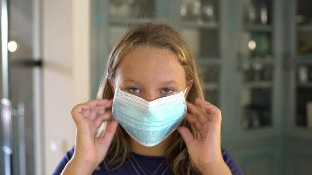 Caucasian teen girl puts on a protective mask at home looking at camera. Concept new rules, new normality during Coronavirus, COVID-19.