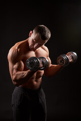 Fototapeta na wymiar Shirtless muscular man holding dumbbells against of black background.Studio shot