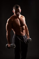 Obraz na płótnie Canvas Shirtless muscular man holding dumbbells against of black background.Studio shot