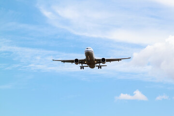 white passenger plane comes in to land with natural background of white clouds and blue sky