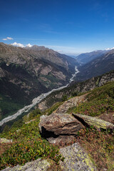 Large-scale mountain landscape from the height of the mountains. A small river in the distance and a lake. Cloudy blue sky.