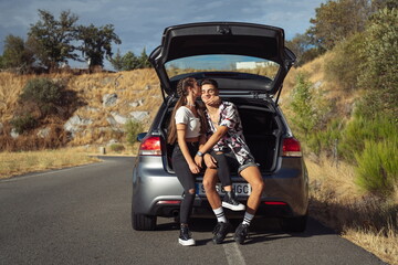 Couple sitting in car boot while waiting for tow truck to arrive