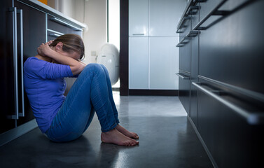 Depressed young woman, sitting on the kitchen floor, feeling down