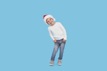 Portrait of a satisfied little child boy dressed in christmas Santa hat. laughing isolated over blue background