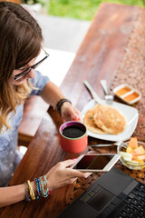 Woman using laptop and cellphone at home during breakfast - freelancing concept.