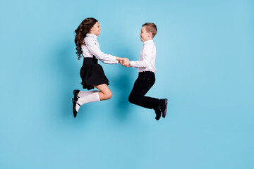 Full length profile photo of two opposite small girl boy schoolchildren brother sister classmates jump hold hands having fun wear white shirt black pants dress isolated blue color background