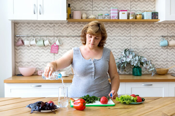 Woman plus size pours water into a glass in her kitchen.