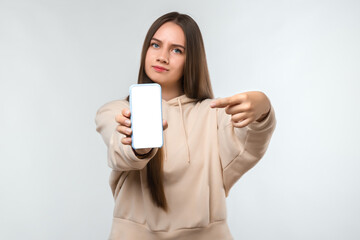 Portrait of pretty girl pointing finger at blank screen mobile phone isolated over white background