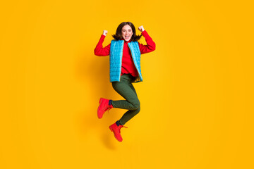 Full length photo of ecstatic girl jump raise fists celebrate season discount lottery wear green blue red sweater clothes isolated over bright shine color background