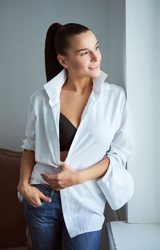 Woman in unbuttoned shirt smiling while looking through the window.