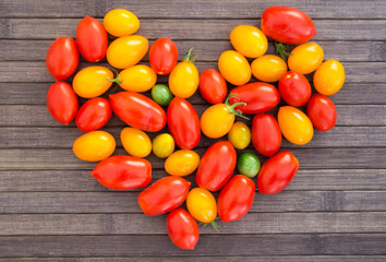 heart made of bright ripe yellow and red cherry tomatoes with place for inscription on wooden table