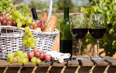 still life with glass of red wine grapes and picnic basket on table