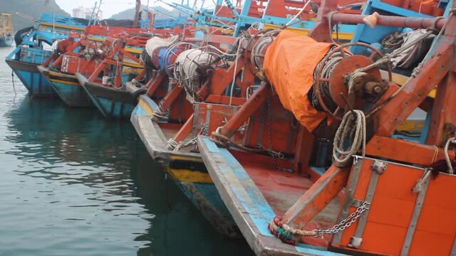 Fishing trawler at the pier lined up side to side (stern and winch), the bright colors of the ships. Vietnam, South China sea
