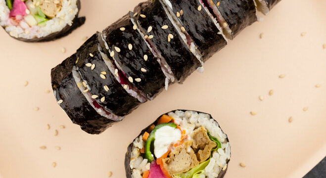 Top view plated Korean traditional sliced kimbap made with tuna, kimchi, purple marinated radish, mayonnaise sauce, carrot, lettuce, rice and seaweed and sesame seeds with empty copy space.  