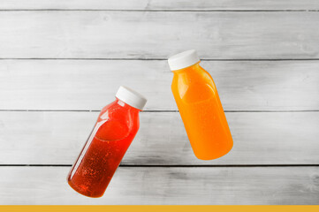 two transparent bottles of bright red and orange non-alcoholic detox drink with white closed lid with the effect of levitation against light wooden wall