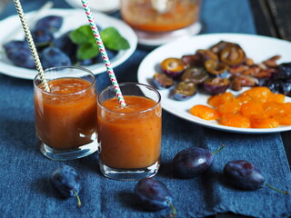 Dark background with glasses of orange juice on a blue napkin.Juice or smoothie made from natural plum with ingredients for cooking.