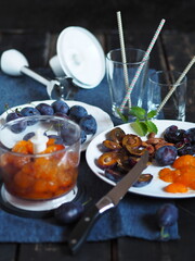 Dark background with a blue ripe plum on a blue napkin. The process of making creamy juice from natural plums or smoothies using a mixer.