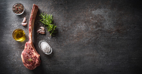 Raw tomahawk steak with salt spices garlic and herbs on a old rustic board - Top of view