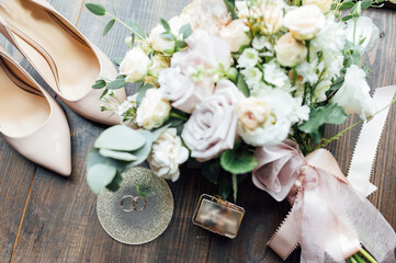 Luxurious wedding bouquet next to the rings of the bride and groom. The bride's shoes with heels