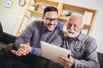 Adult son and his senior father with tablet at home.