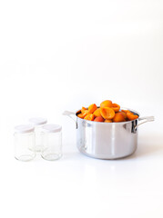 Marillen im Topf mit Einmachgläsern zum Konservieren. Kochtopf vor weißem Hintergrund. Apricots in a pot with preserving jars for homemade jam. Apricots in a pot against a white background.