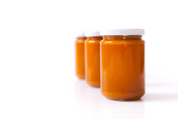 Selbstgemachte Aprikosen-Konfitüre im Glas vor weißem Hintergrund. Marillenmarmelade selbst gemacht. Homemade apricot jam. Homemade apricot jam in a glass against a white background. 