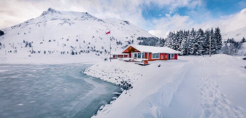 Traditional Norwegian red wooden houses on the shore of frozen fjord. Bright winter scene of Lofoten islands on the shore of Kongsjordpollen fjord, Vestvagoy, Norway, Europe. Life over polar circle.