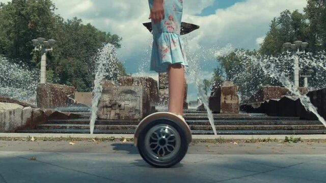 A hoverboard in motion, slow motion, the girl is rolling around. Rest on a day off in the park outside. against the background of a large fountain.