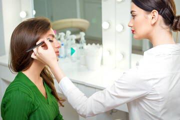 Obraz na płótnie Canvas Makeup artist applies eyeshadow powder on eyes of young caucasian woman by brush tool in beauty salon