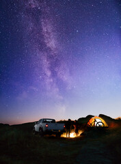 Friends near Bonfire, Pickup Truck, Tent and Bike in the Mountains under Night Sky with Milky Way....