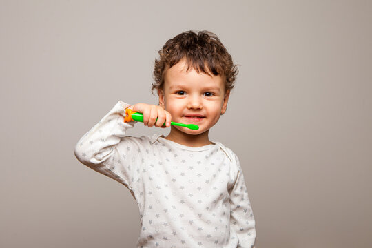 funny curly kid stands smiling and holds a toothbrush in his hands. Healthy strong children's teeth. The rules of personal hygiene. white background, isolated