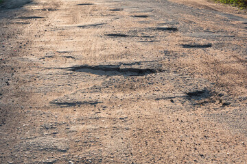 A fragment of an old asphalt road with a badly worn surface. There are deep pits with uneven edges. Background. Texture.