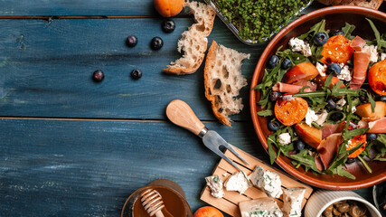 Easy recipe for summer salad with goat cheese, grilled apricots, arugula, prosciutto, berries, close-up on a plate wooden background, recipe top view
