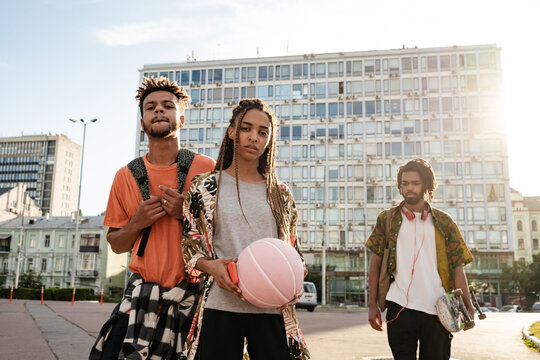 Teenage friends walking outdoors with ball and skateboard