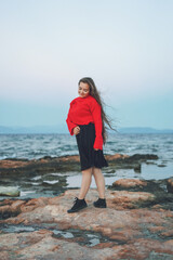 Portrait of a happy joyful woman wearing a red sweater in the beach in a cloudy windy evening near the sea