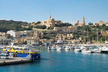 Fototapeta na wymiar The ferry from Malta to Gozo island goes to the picturesque harbor of Mgarr port where the luxury yachts and traditional fishing boats are staying