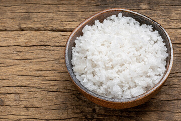 Natural sea salt in a ceramic bowl on wooden background