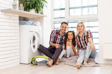 family mother, father and child girl little helper in laundry room near washing machine and dirty clothes