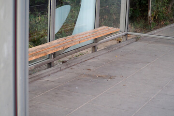 an empty stop with glass walls and a wooden seat for public transport in Europe in the early morning