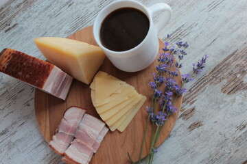 Morning breakfast, coffee, cheese and meat on a wooden stand on the table.