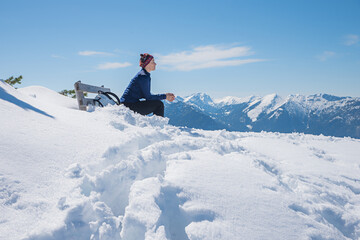 Fototapeta na wymiar young woman sitting on a bench in snowy landscape, Wank mountain summit