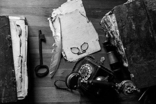 
An old sheet of paper, an envelope, a postcard on a desk and vintage accessories and antiquity writing items. Top view, black and white image