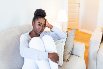 Sad thoughtful worried african american girl sit on sofa looking away feel depressed doubtful, lonely stressed upset young black girl thinking of psychological problem thinking regret about mistake