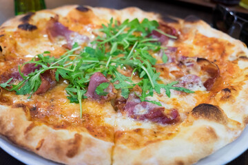 Homemade pizza with ham, chorizo sausage, tomato sauce, mozzarella cheese and arugula 