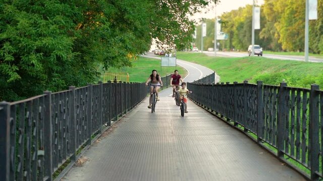 Fit family on cycle biking in summer. Tracking shot mother, father and son riding bicycles across metal bridge with forged fence. Concept of sport