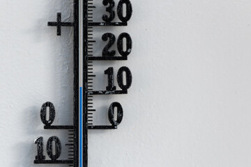 Classic analog thermometer hanging on white wall displaying warmth of twelve degrees celsius