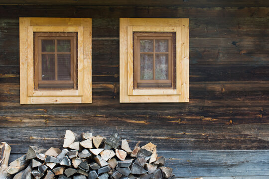 Two windows on a wooden house and chopped wood in front of it. Wood texture. The countryside.
